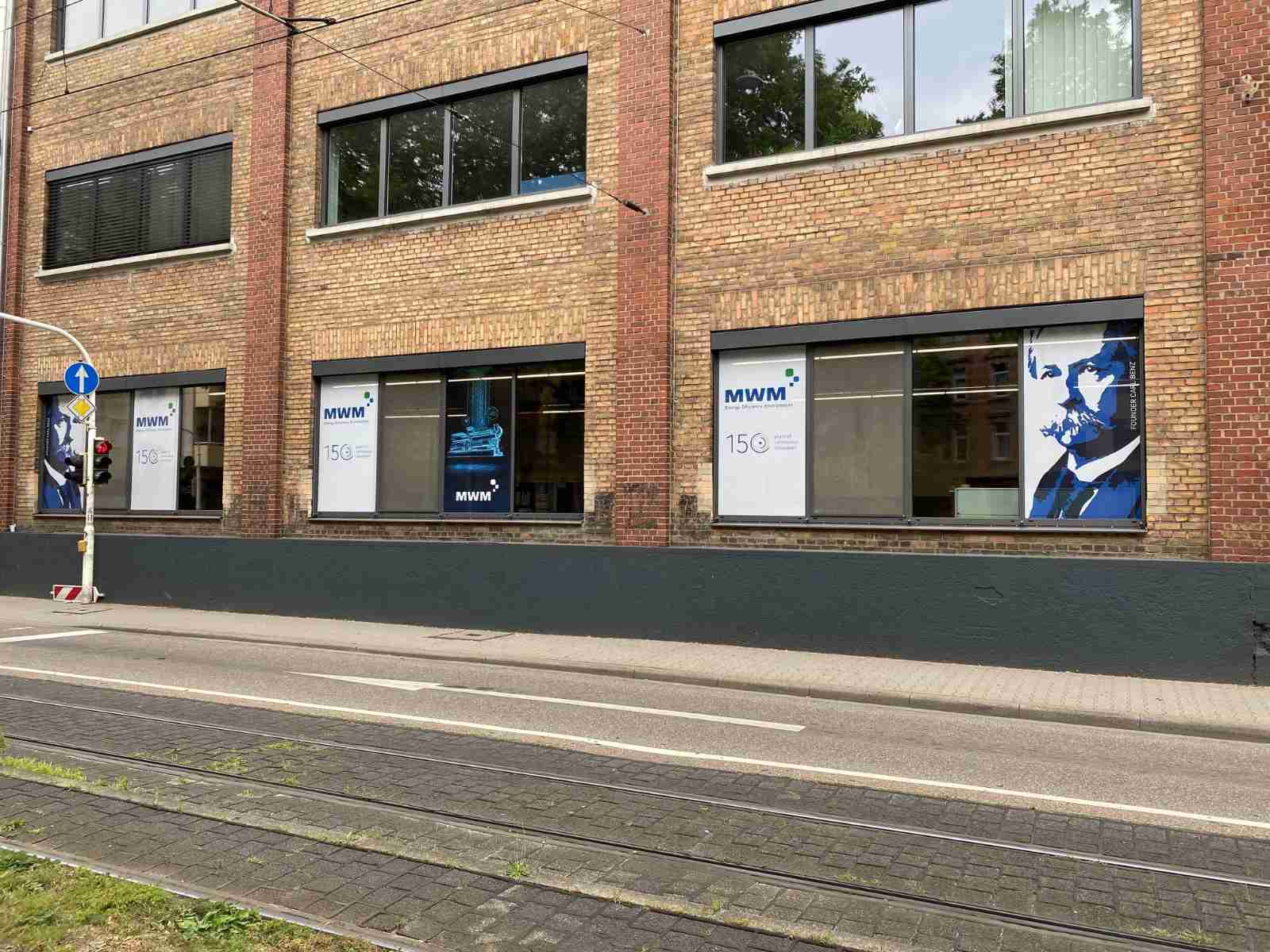 Окна, выходящие на Вальдхофштрассе и Карл-Бенц-Штрассе, с плакатами, изображающими основателя компании Карла Бенца и газовый двигатель TCG 3016 MWM